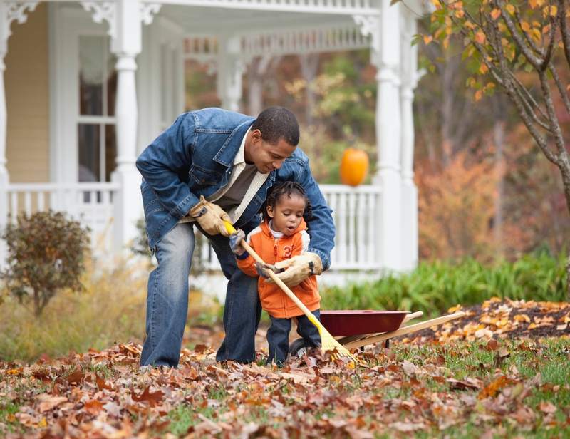 Father and son rake leaves after buying a home in the fall.