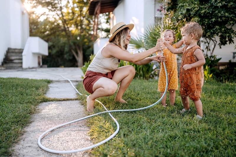 Mother and children play with hose after buying home in summer.