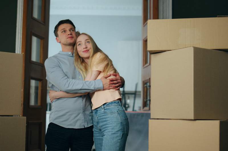 Couple embraces amid moving boxes in the doorway of their new home.