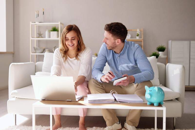 A woman and a man sit on a sofa reviewing their finances on a computer.