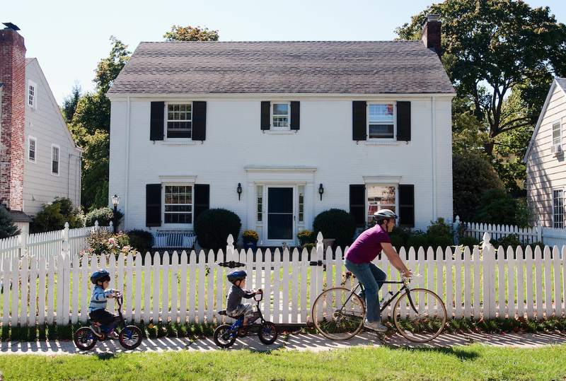 Father and sons bicycle past a single-family house.