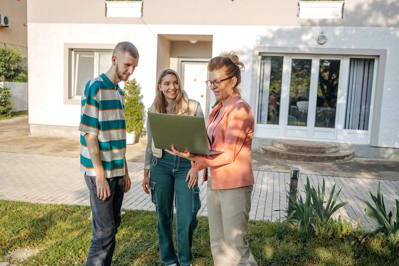 Couple and agent consult a laptop in the backyard of a home for sale.